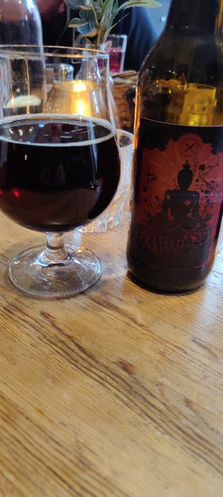 Ett glas mörk öl och en flasketikett från Klövsjö Gårdsbryggeri på ett träbord.