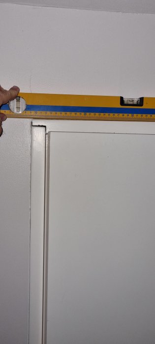 En hand håller en gul vattenpass över en dörrkarm för att kontrollera dess lodräthet.