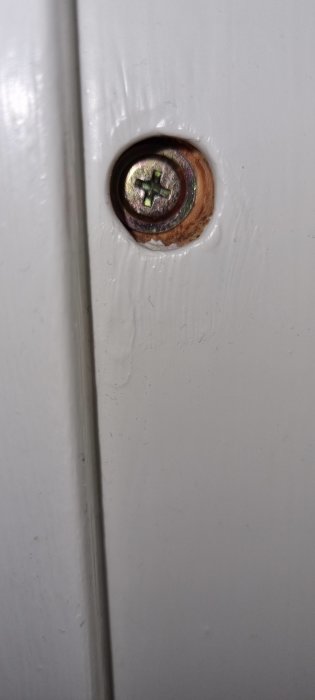 Skruv med tecken på korrosion i fästpunkt på vit dörrkarm.