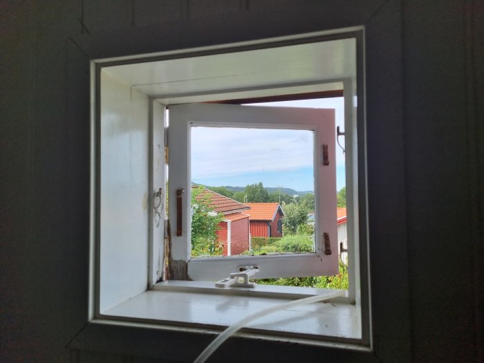 Utsikt från ett öppet fönster som visar en trädgård och ett landskap i bakgrunden.