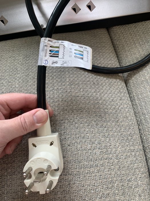 Eluttag med anslutningskabel och märkning för olika spänningar hållen av en hand.