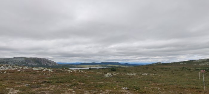 Öppet fjällandskap med molnig himmel, markerad ledd och en sjö i fjärran.