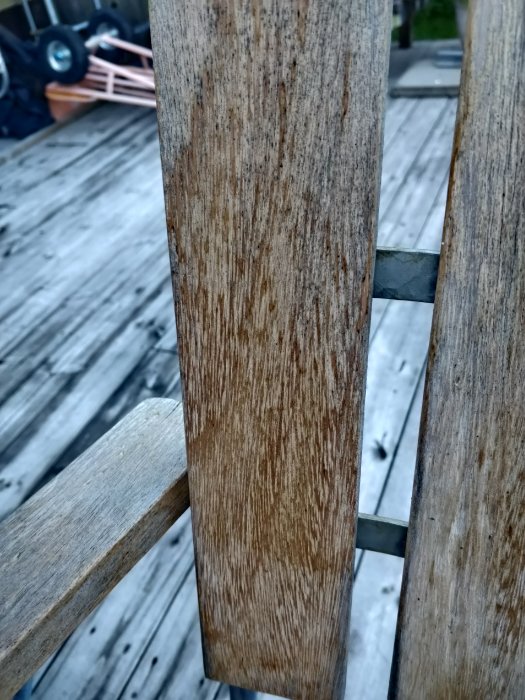 Närbild av väderbitna ekbrädor på en Grythyttan-stol mot suddig bakgrund av trädäck.