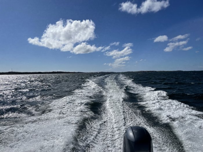 Vy från en båt som färdas på vattnet med vågspår efter sig och blå himmel ovan.