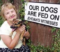 Kvinna ler och håller en hund intill en skylt som säger "Our dogs are fed on Jehovah's Witnesses".