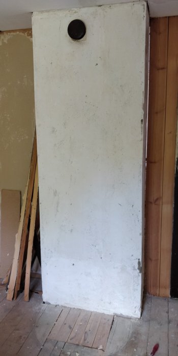En gammal vit dörr stående i ett rum under renovering, med synligt slitage och fläckar.