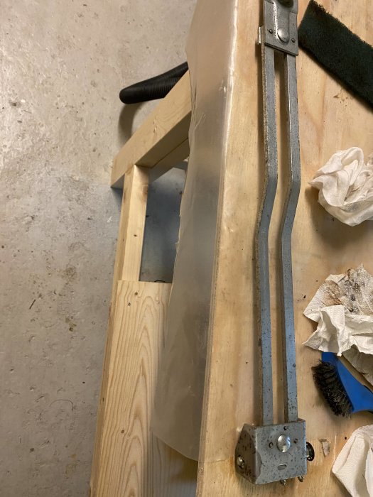 Riktbord i trä med oljefläckar och en rostangripen metallarm, omgiven av rengöringsverktyg.