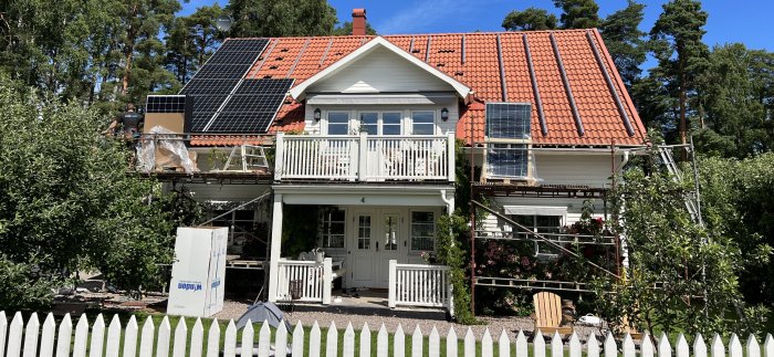 Installation av solpaneler på taket av ett vitt hus med orange tegeltak och balkong.