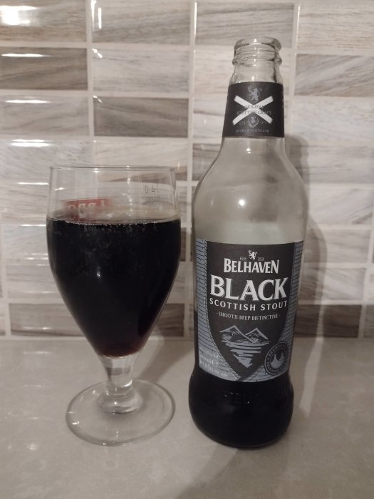 En flaska och ett glas fyllt med mörk stout öl, märkt Belhaven Black Scottish Stout.