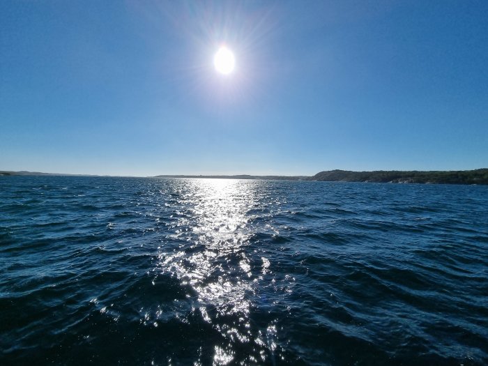 Solreflektioner på havsvatten med klarblå himmel och solen i bild.