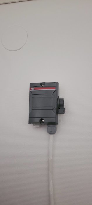 En ABB-strömbrytare kopplad till en vägg med en lösgjord kabel vid botten.