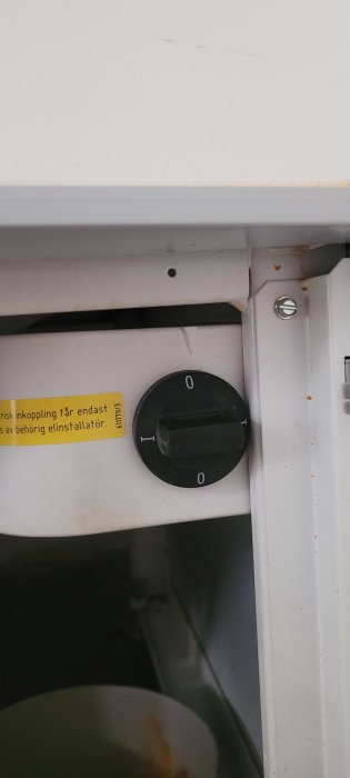 Strömbrytare i "av" läge under diskbänk, varningsetikett samt otydlig bakgrund.