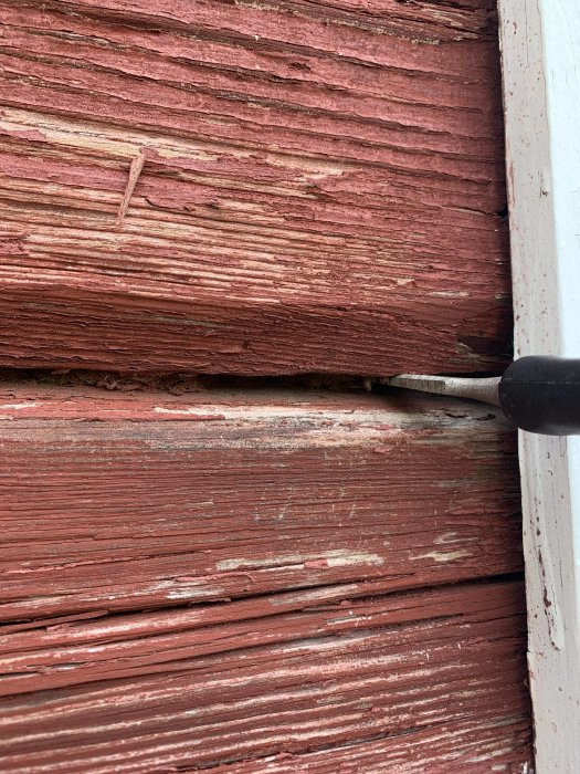 Närbelde på en rödmålad trävägg med en stämjärn insatt i en glipa mellan panelbrädor.