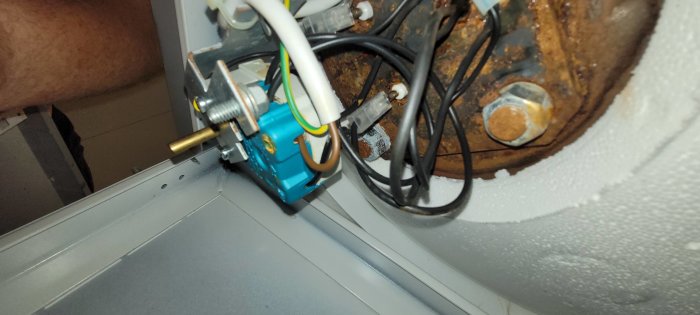 Elanslutningar och termostat på en varmvattenberedare med rost och isolering i förgrunden.