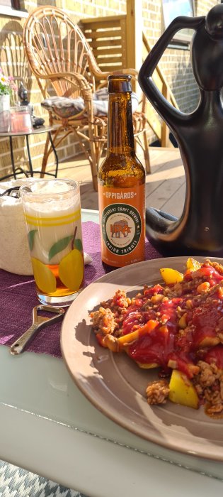 Tallrik med chili con carne, ölflaska och glas öl på ett uteserveringsbord i solen.