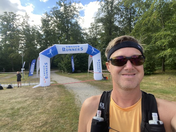 Person i löparutrustning tar selfie framför målgångsbåge med texten "SWEDEN RUNNERS".