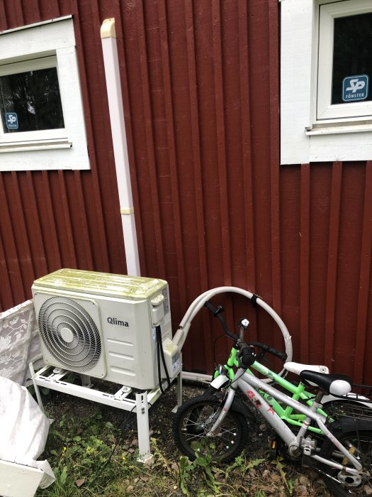 Luftvärmepump placerad utomhus bredvid ett fönster med barnens cyklar lutade mot den.