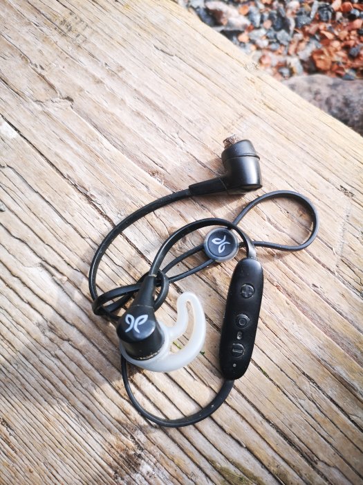 Jaybird X4 trådlösa hörlurar med mjuka vingar och Comply skumkuddar på träyta.