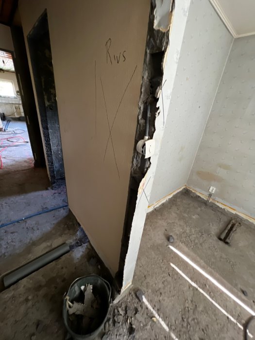 Delvis nedriven lättbetongvägg med synlig elinstallation och ordet "Rivs" skrivet på väggen, rivningsavfall i hink.
