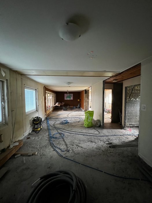 Renoveringsarbete med borttagna väggar, synliga elledningar på golv och verktyg i ett halvtomt rum.