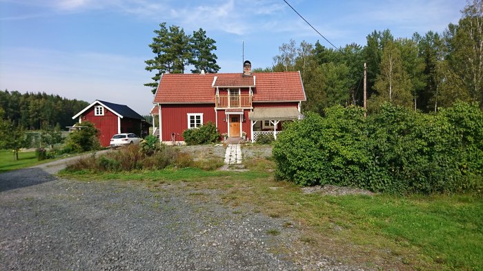 Rött traditionellt hus med vita knutar och grönskande trädgård på landsbygden.