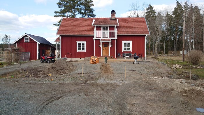 Röd trävilla med vita knutar och pågående anläggning av trädgård framför huset.