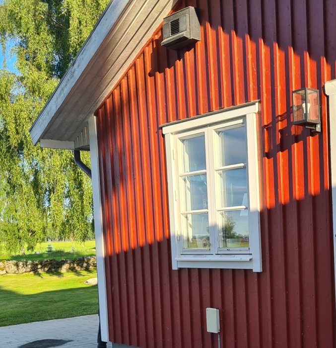 Rödmålad husvägg med blankare röda nyanser, vita fönster och solskuggor.