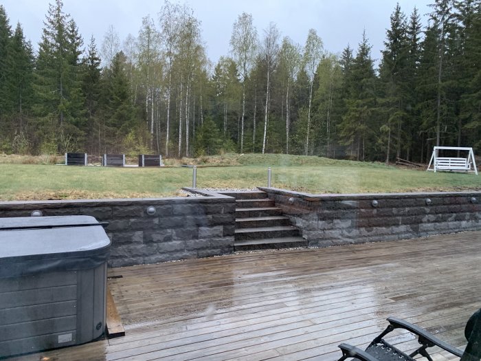 Trädgård med stenmur, trätrappa och uteplats under lätt snöfall.