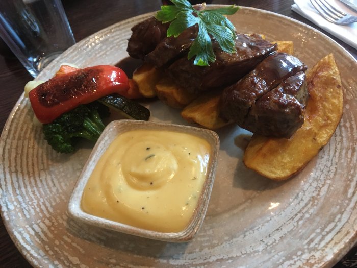 Black Angus-steak med klyftpotatis, bearnaisesås och grillade grönsaker på en restaurangtallrik.