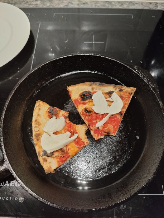 Två bitar pizza som återuppvärms i en gjutjärnspanna på spishäll.
