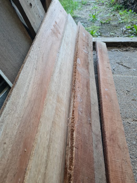 Stapel av olika typer av obehandlade träplankor lutade mot en vägg.