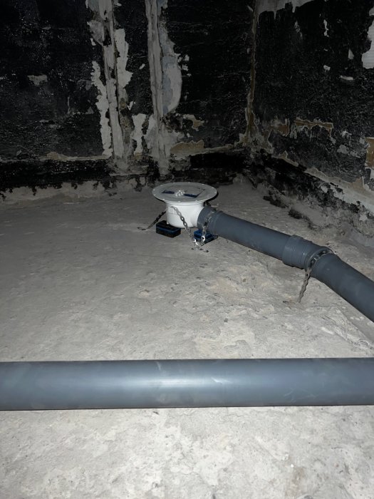 Installation av avloppsrör med gummimuff, 45° böjar och fastsatt brunnskoppling i en källare.