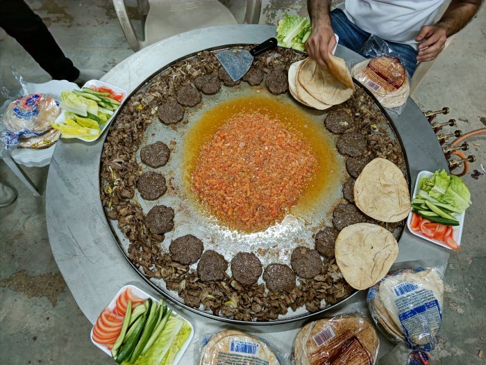 Stor stekpanna med lammfett, lammkött, kryddor och pitabröd omgiven av färska grönsaker.