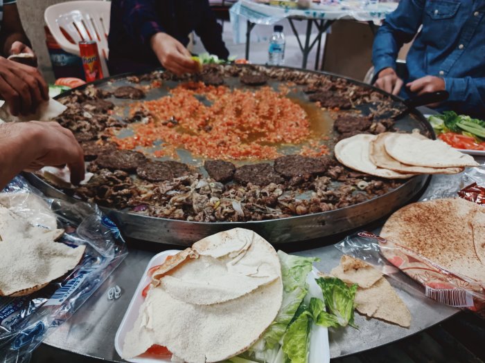 Stort grillerat lammkött och grönsaker på en plåt med arabiskt bröd och sallad runt omkring.