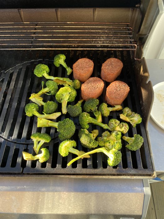 Grill med vegetariska biffar och färsk broccoli på varm grillrist i solljus.