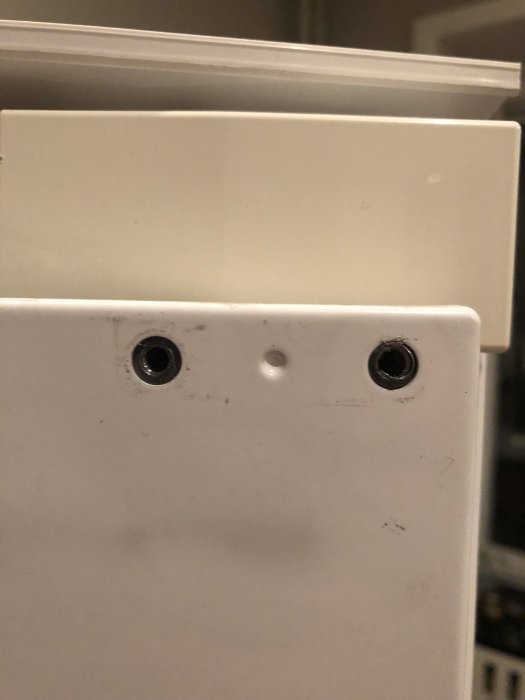 Närbild av en vit dörr med två hål som ser ut som ögon och ett mindre hål som ser ut som en näsa.