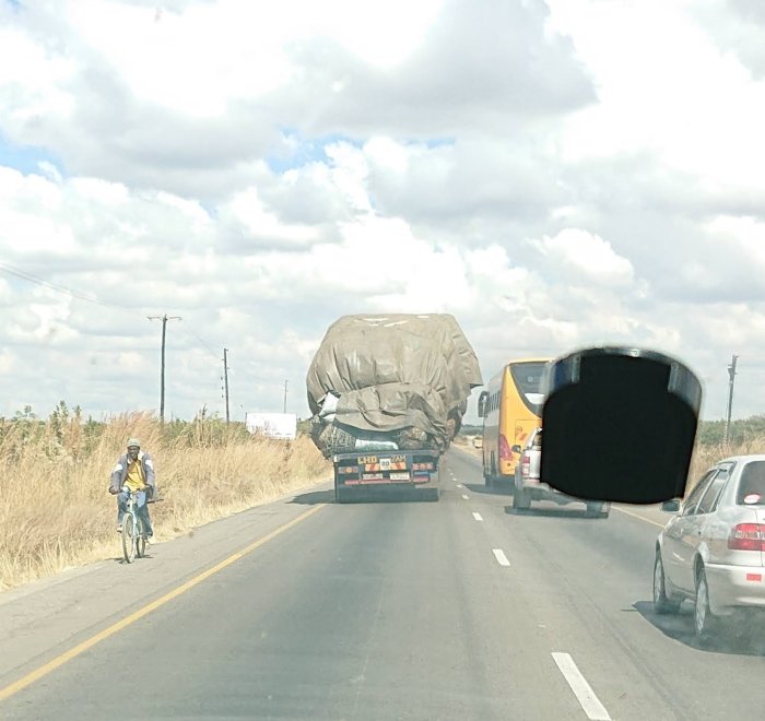 Överlastad lastbil med presenning på väg i Zambia, sidosurrad, med andra fordon och cyklist.