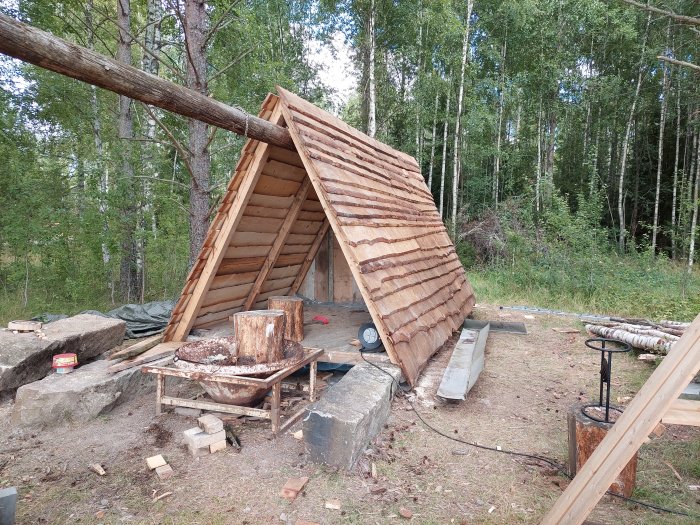 Nästan färdigbyggd träkonstruktion av tak med bräder i en skogsmiljö, väntar på nockplåt.