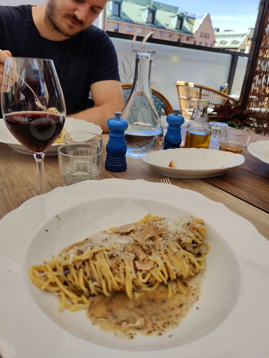 Person äter pasta med kaviar på en italiensk restaurangs terrass, med vin och vatten på bordet.