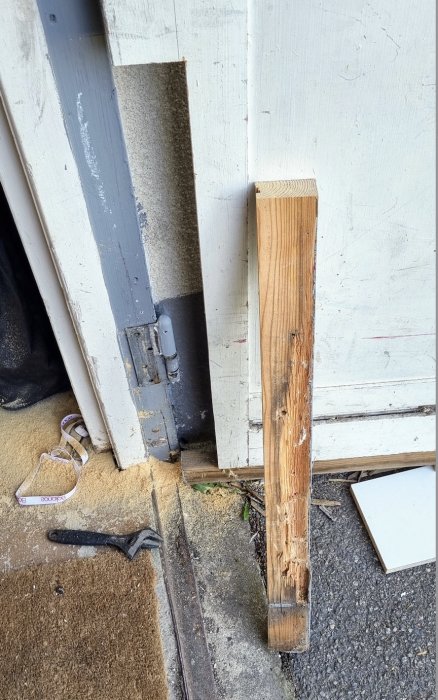 Reparation av en dörr med utbytt trästycke och synligt gammalt, skadat trä vid gångjärnet.