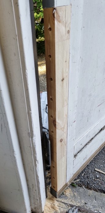Ny träbit monterad på dörr för att reparera skadad del, limmad och skruvad.