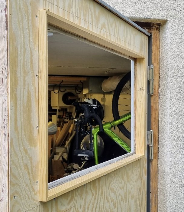 Ny plywoodbeklädd dörr med ny infattning och fönster, synligt cykelförvaringsutrymme bakom.