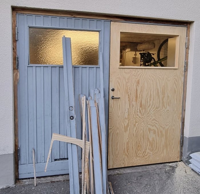Två dörrar, en klädd med plywood och den andra med gammal blå panel. Renoveringsmaterial framför.
