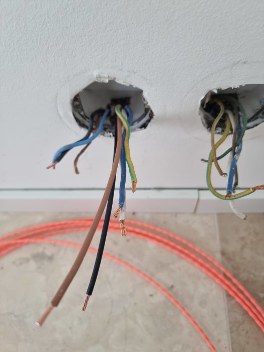 Eluttag utan frontplatta med synliga ledningar i en vägg och korrugerad rör på golvet.