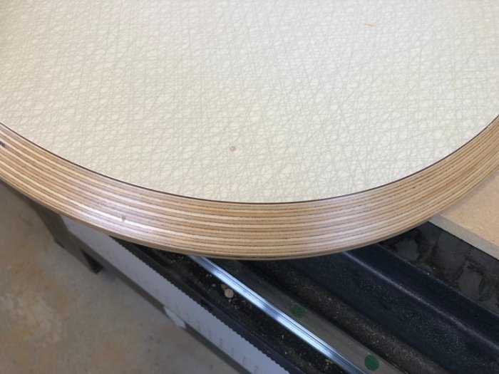 Detalj av ett hörn på en superellipsformad bordsskiva i plywood, ovanpå en CNC-fräsbädd.