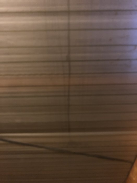 Otydlig närbild av trätextur med mörk längsgående skugga eller teckning på ytan.