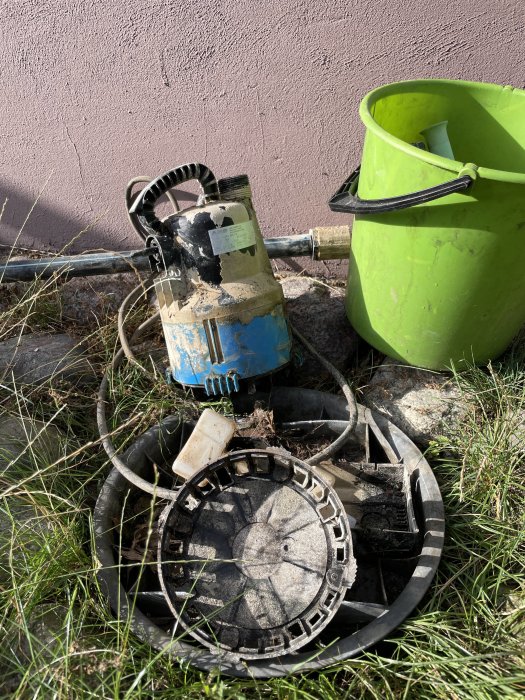 Före detta vattenpump och grön hink som används vid ett renoveringsprojekt, står mot en rosa vägg.