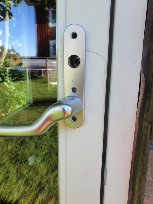 Närbild av en vit ytterdörr med en nyinstallerad dörrhandtag och lås i silverfärgat utförande.