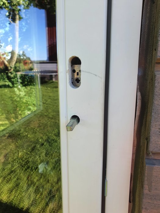 Vita ytterdörrens karm med borstad urtagning för låset och ett synligt låscylinderhål.
