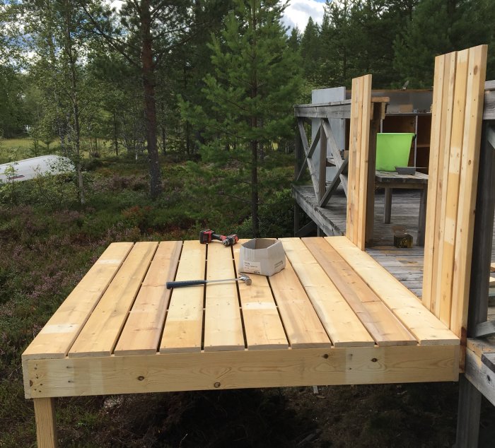 Nybyggt träbjälklag för utbyggnad vid ett torp med skogsbakgrund, verktyg ligger på konstruktionen.